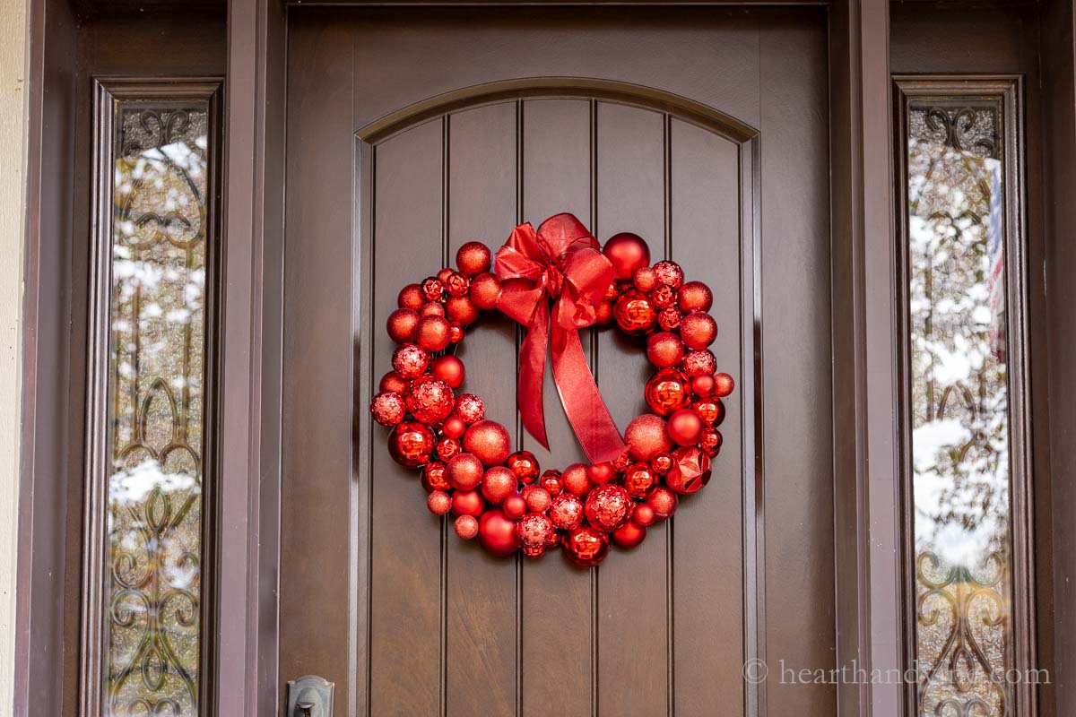 A red ornament wreath hanging on a brown front door.