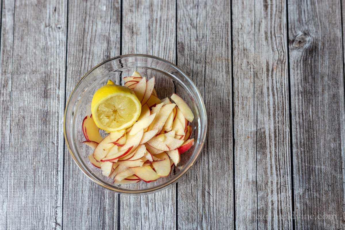 Slices of apples in a small glass bowl with half of a lemon.