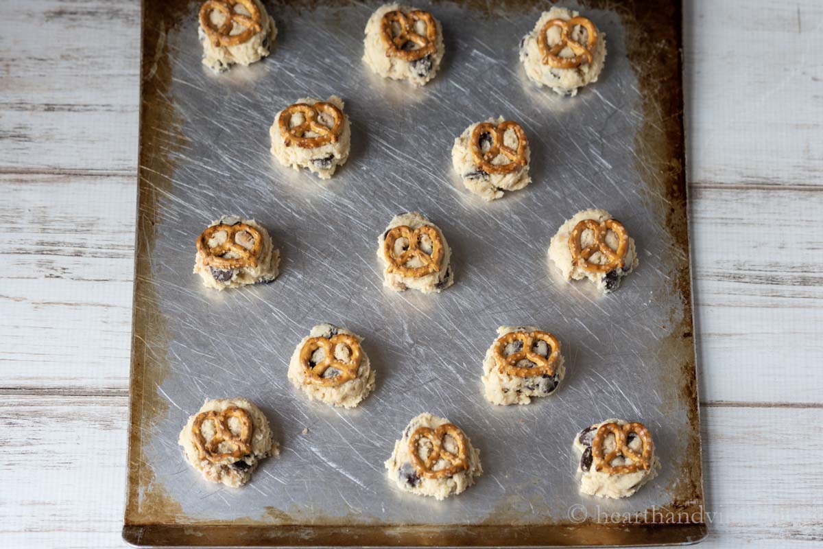 Cookie dough on a baking sheet with a small pretzel on top.