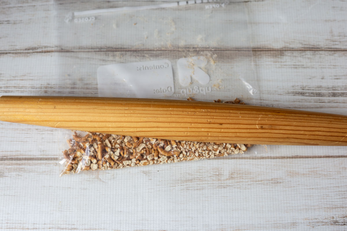 Crushed pretzels in a plastic bag with a wooden rolling pin on top.