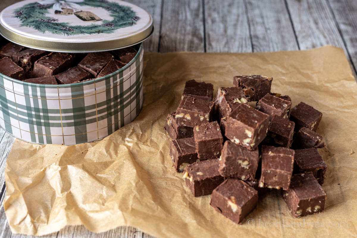 Stacked fudge on parchment next to a holiday tin filled with fudge.