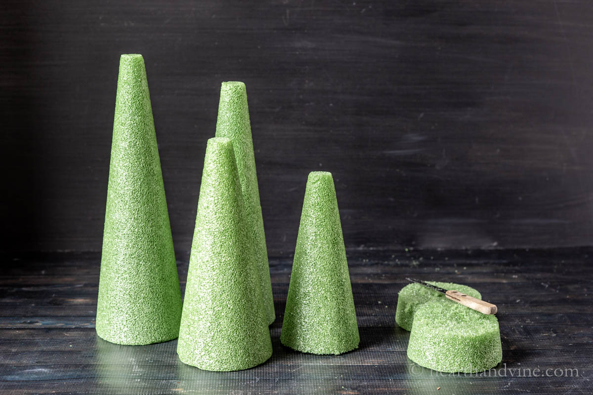 Four green floral foam cones with a portion cut from the bottom and a serrated knife.