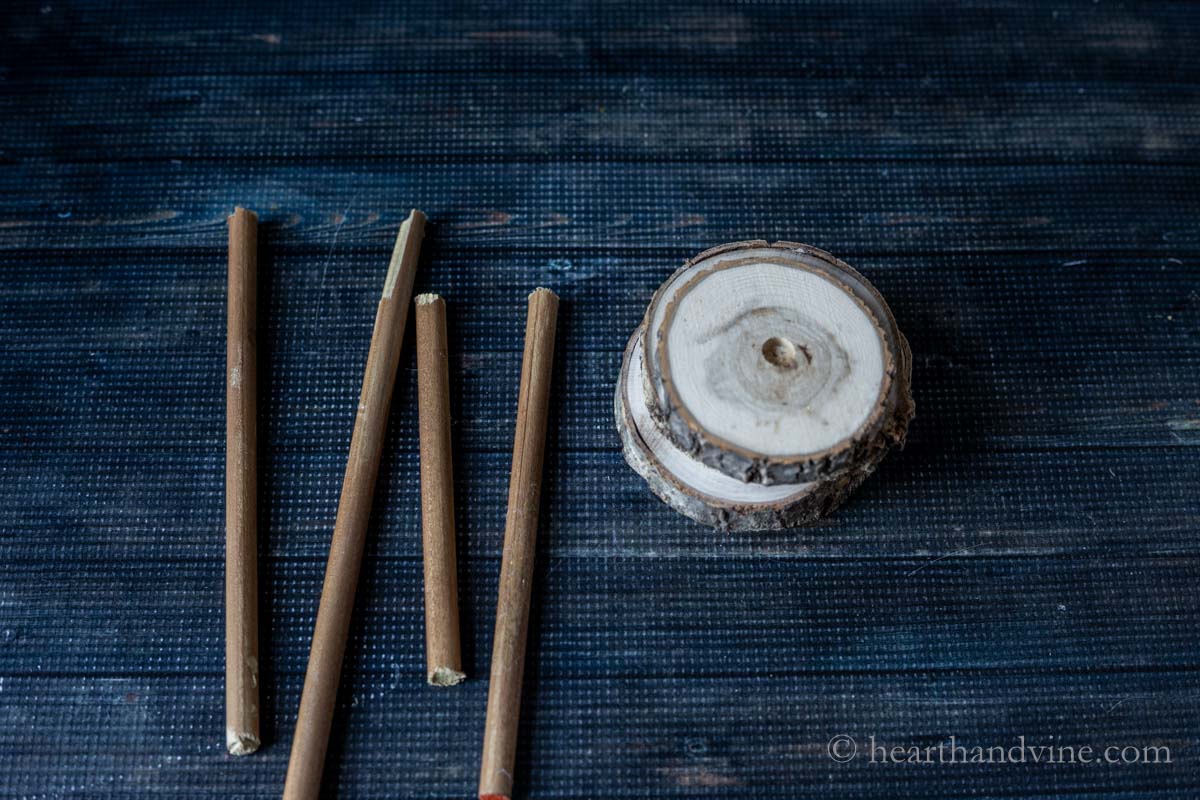 Four brown painted dowel rods in different sizes next to a stack of drilled wood slices.