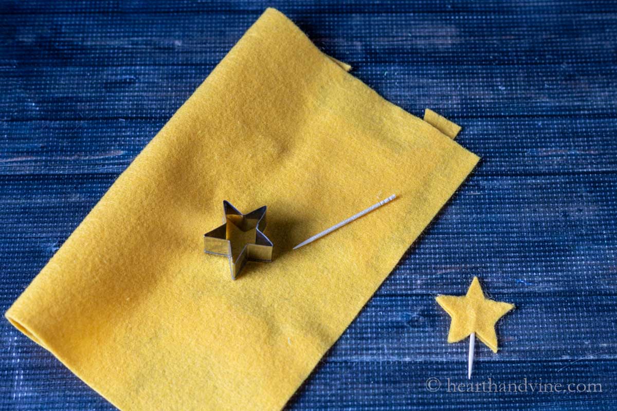 A star shaped cookie cutter on gold felt and a wooden toothpick.