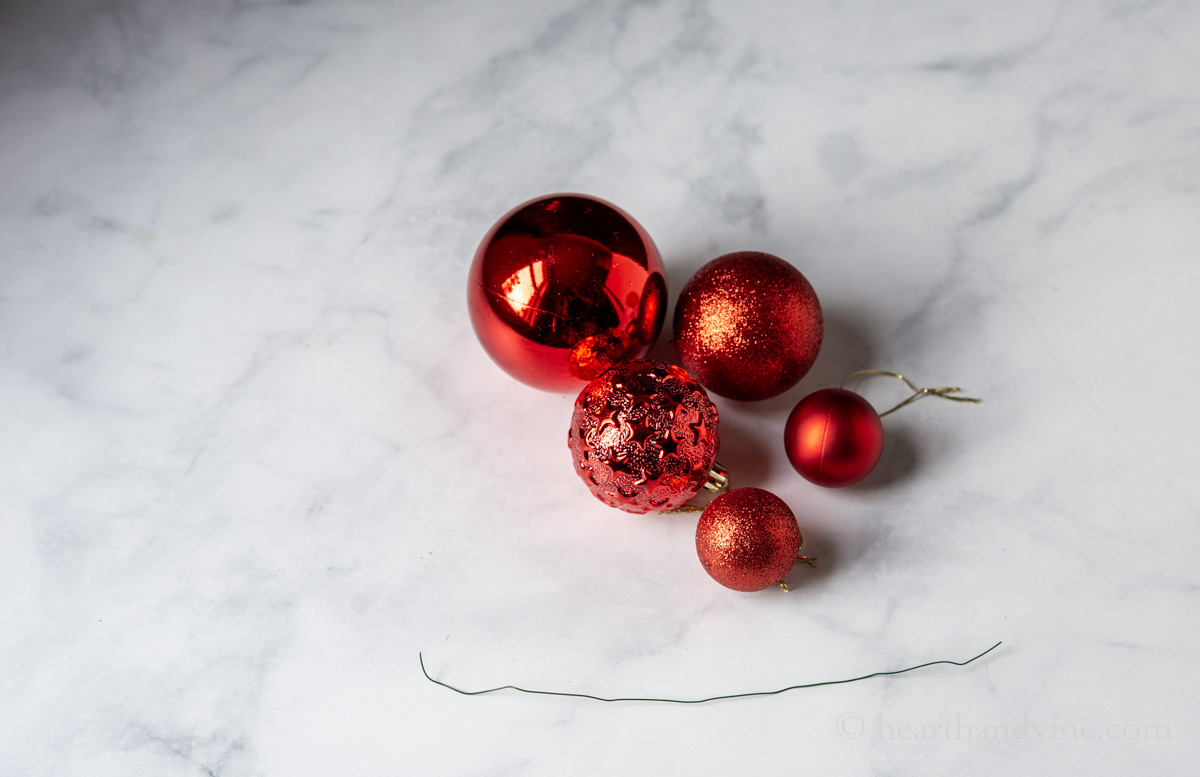 Five different sized and textured red ornaments and a piece of floral wire.