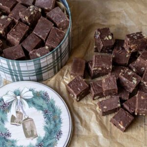 Microwave fudge with nuts in a holiday tin and on parchment to the side.