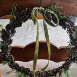 Mini pinecone wreath with green bow on the back of a chair.
