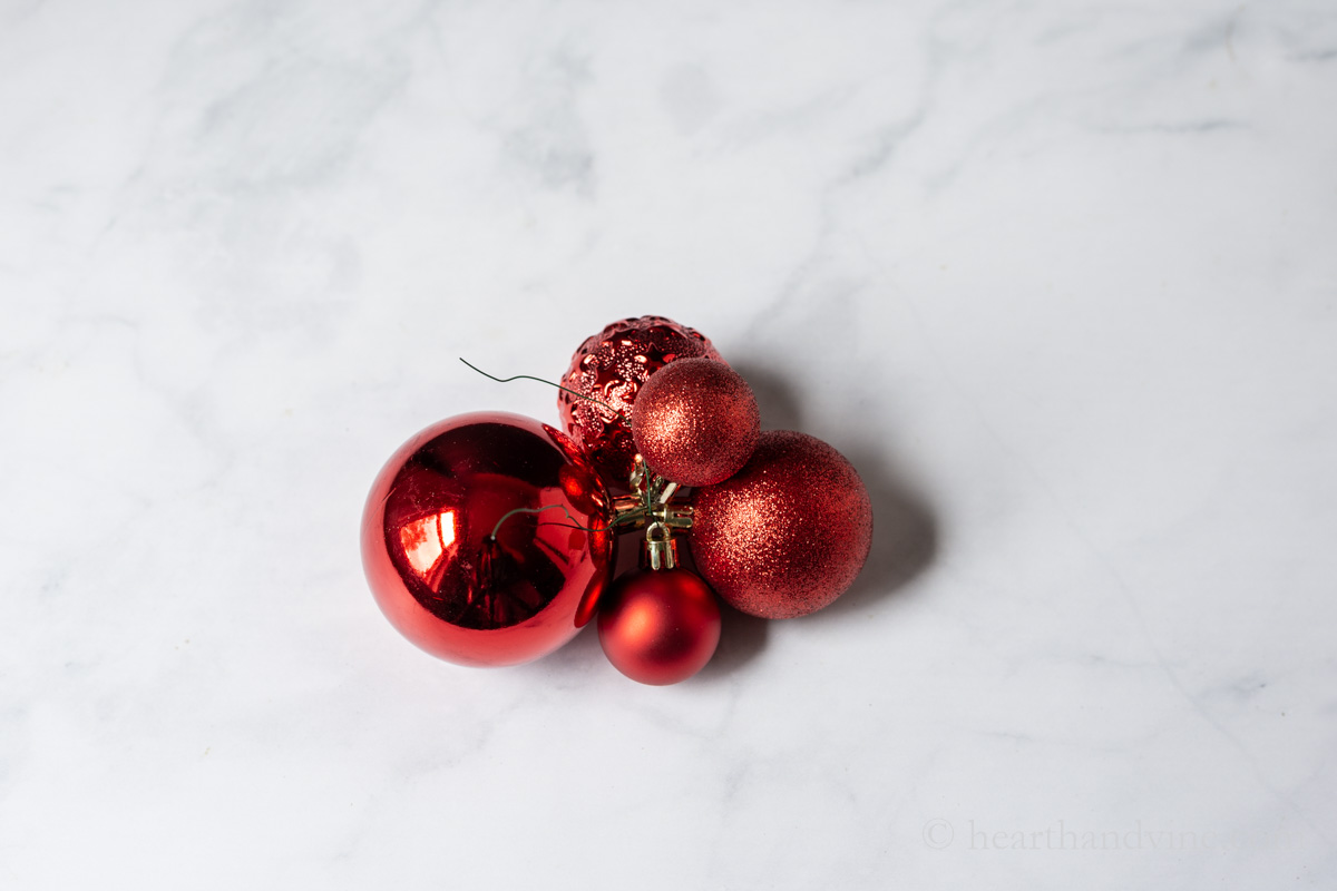 Five different sized and textured red ornament clustered together with green floral wire.