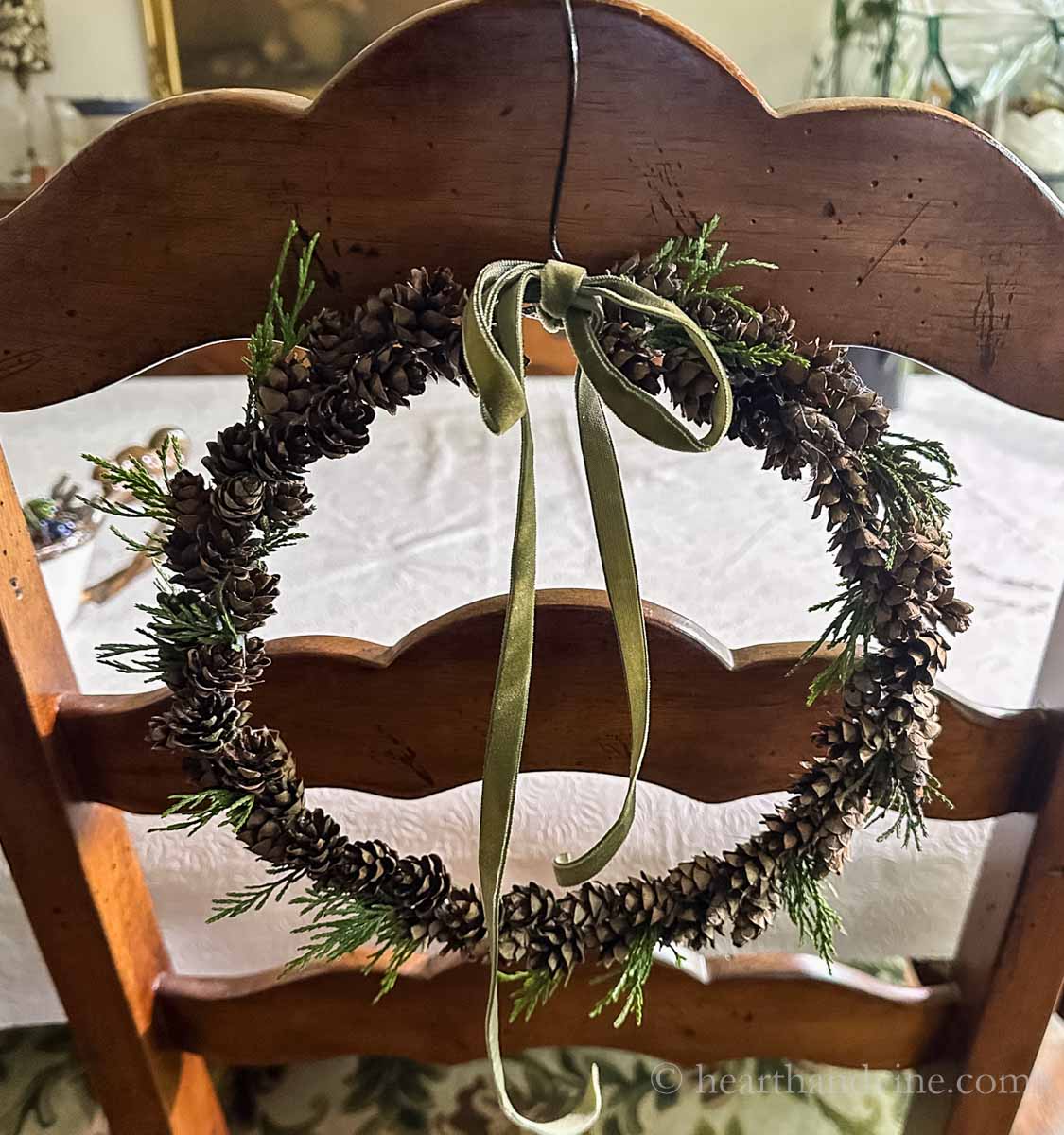 Hemlock pinecone wreath with cedar and green velvet bow on the back of a chair.