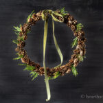 Mini pinecone wreath with cedar and green bow hanging.