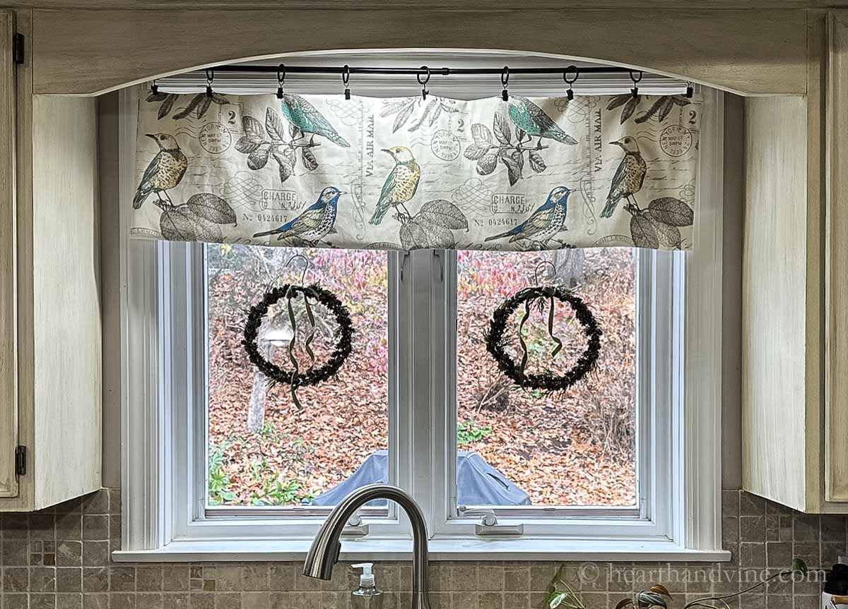 Two pinecone wreaths with green velvet bows hanging in a kitchen window.