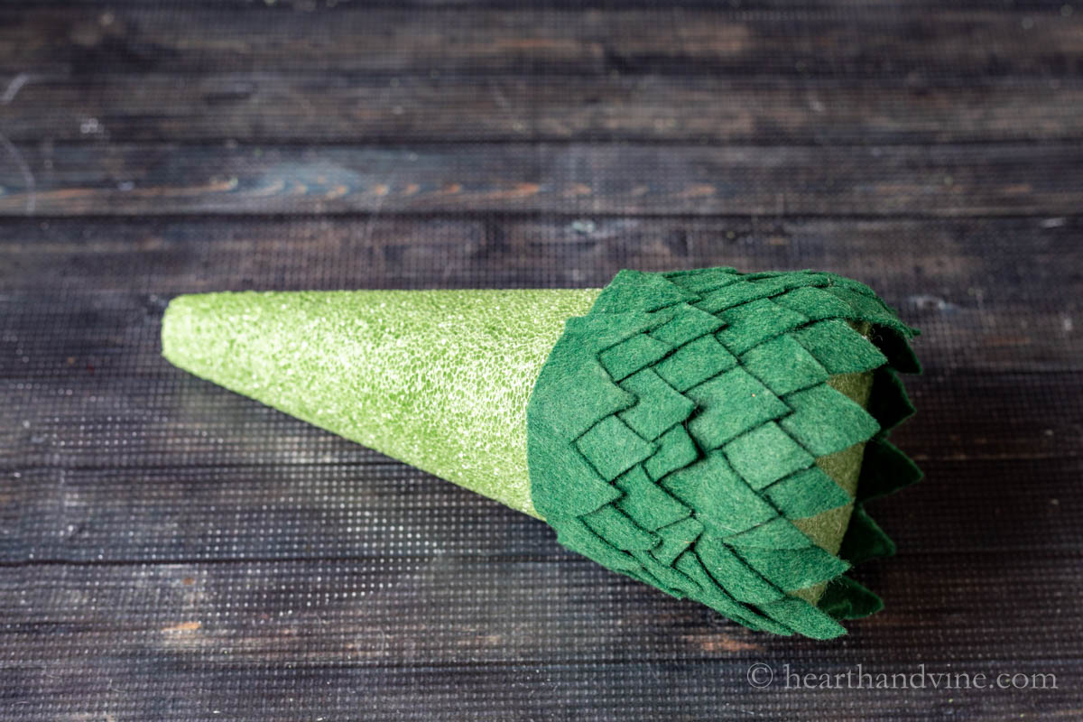 Rows of dark green leaves glued to a green foam cone on the bottom.