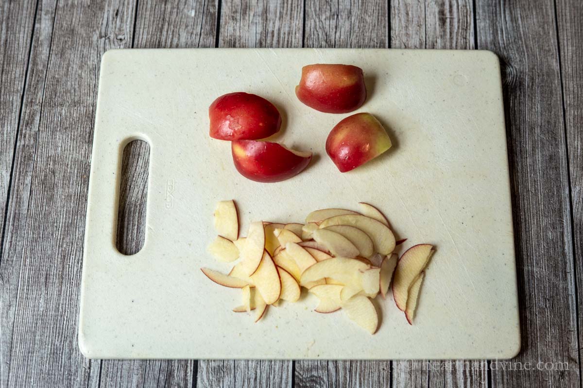Small apple quartered and very thin apple slices on a cutting board.