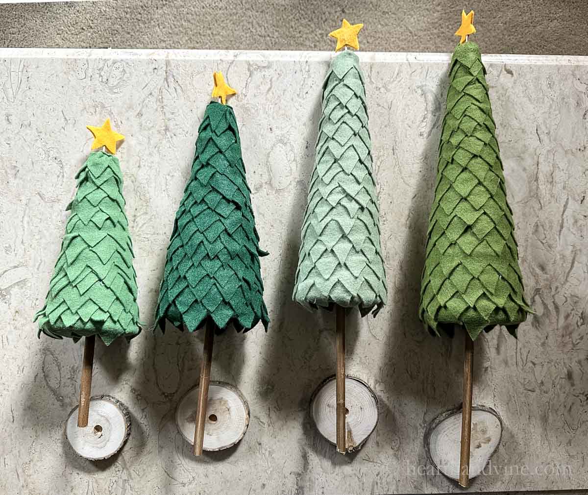 Four felt Christmas trees on a table on their sides with drilled wood slices.
