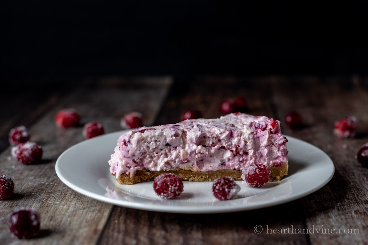 Slice of cranberry cheesecake on a white plate with sugared cranberries scattered around.
