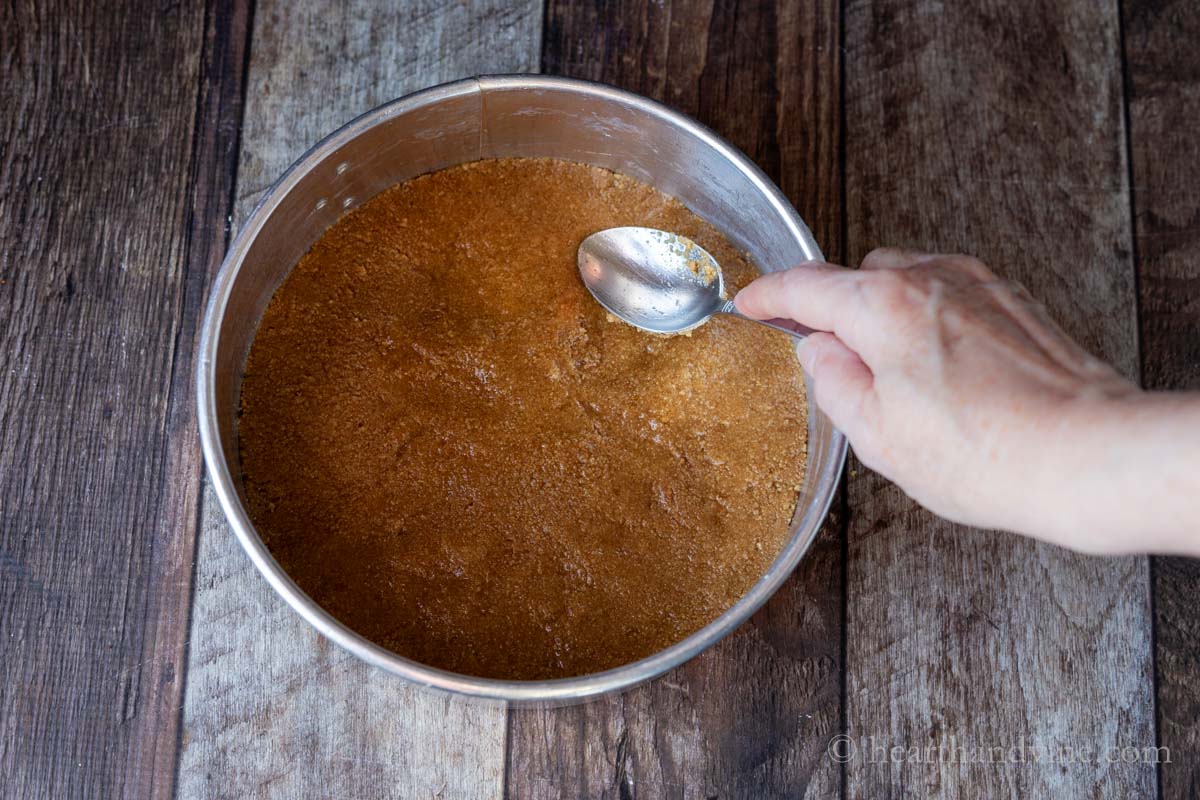 Pressing the graham cracker mixture into a buttered 8-inch springform pan with a spoon.
