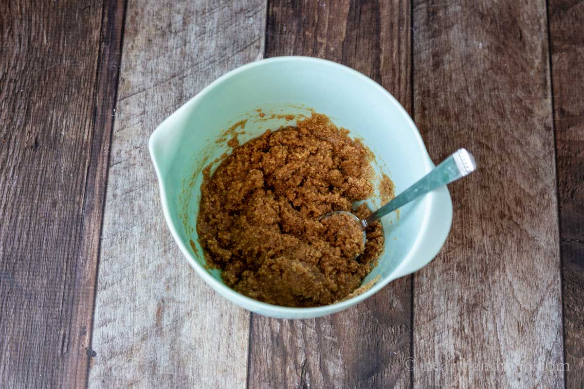 Mixing bowl with graham crackers, sugar, salt and butter with a mixing spoon.