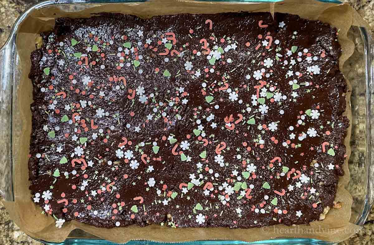 Pan of chocolate fudge with Christmas sprinkle shapes of candy canes, starts, snowflakes in green, red and white.