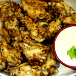 Serving dish of baked chicken wings with a small bowl of blue cheese dipping sauce.