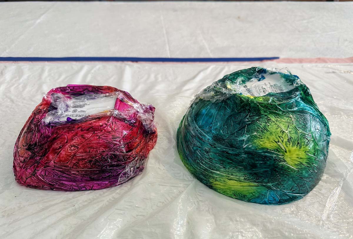 Two ceramic bowls with alcohol inks and plastic wrap upside down.