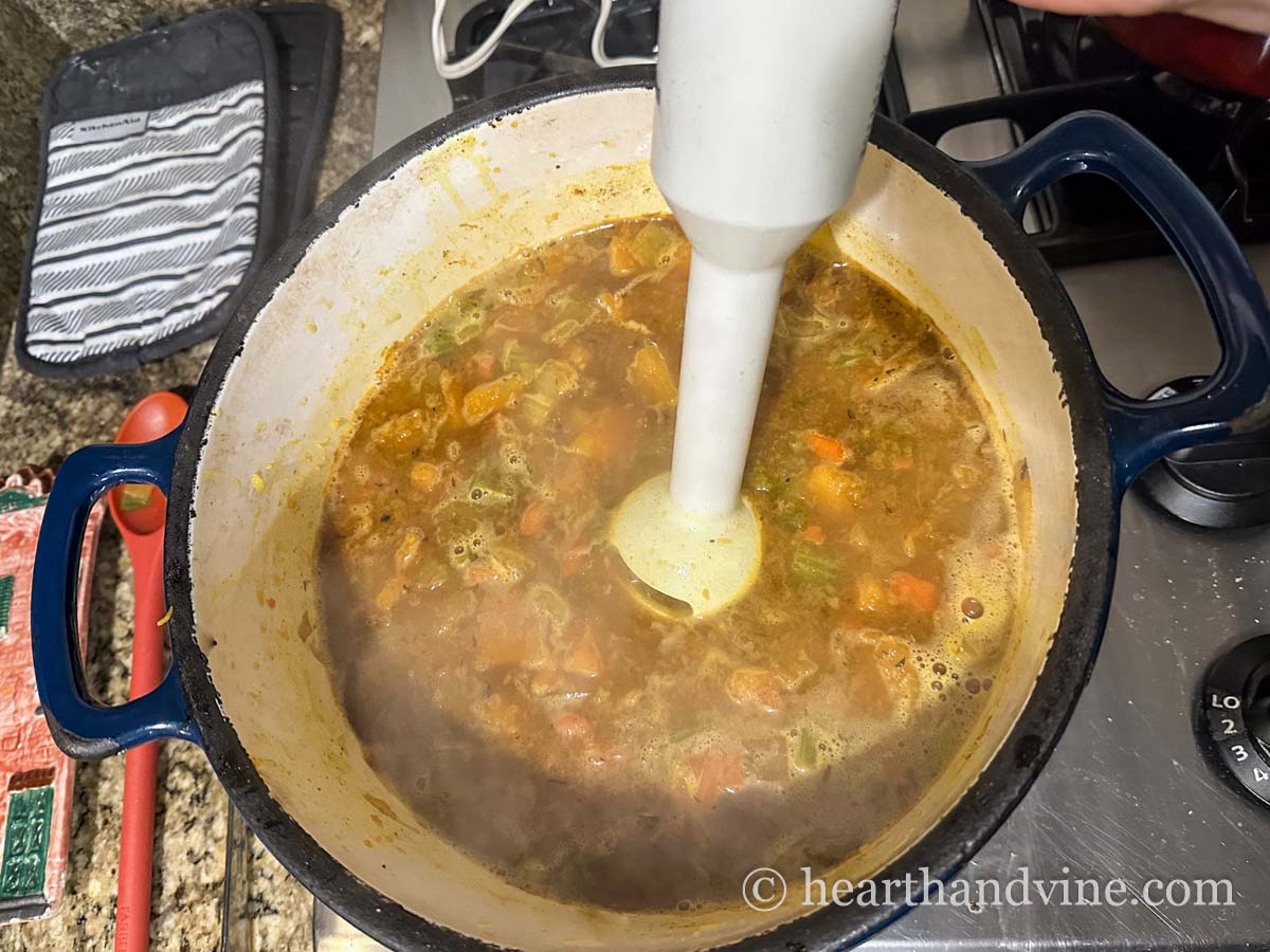 An immersion blender in a large pot of soup making the soup smooth.
