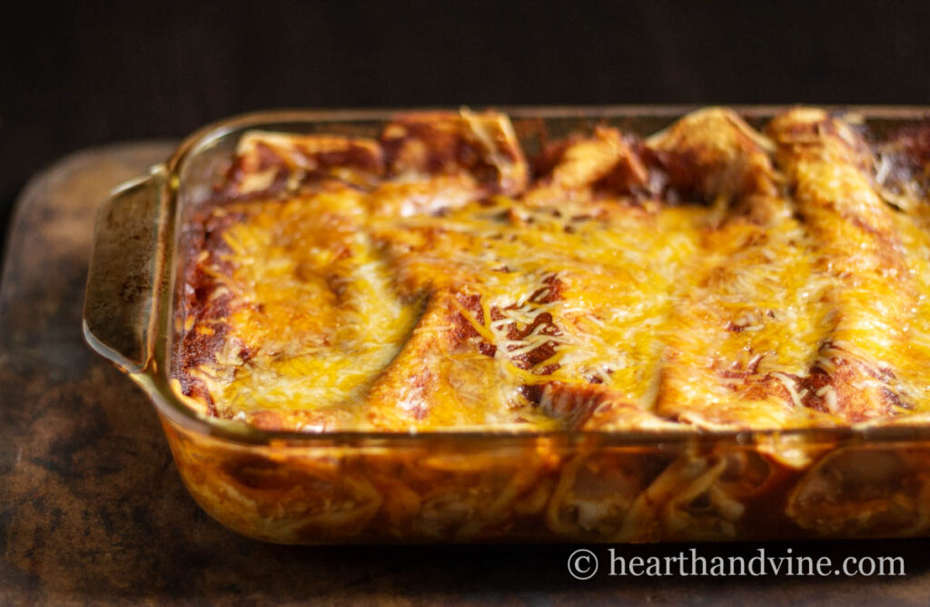 A baking pan with chicken enchiladas and red sauce.