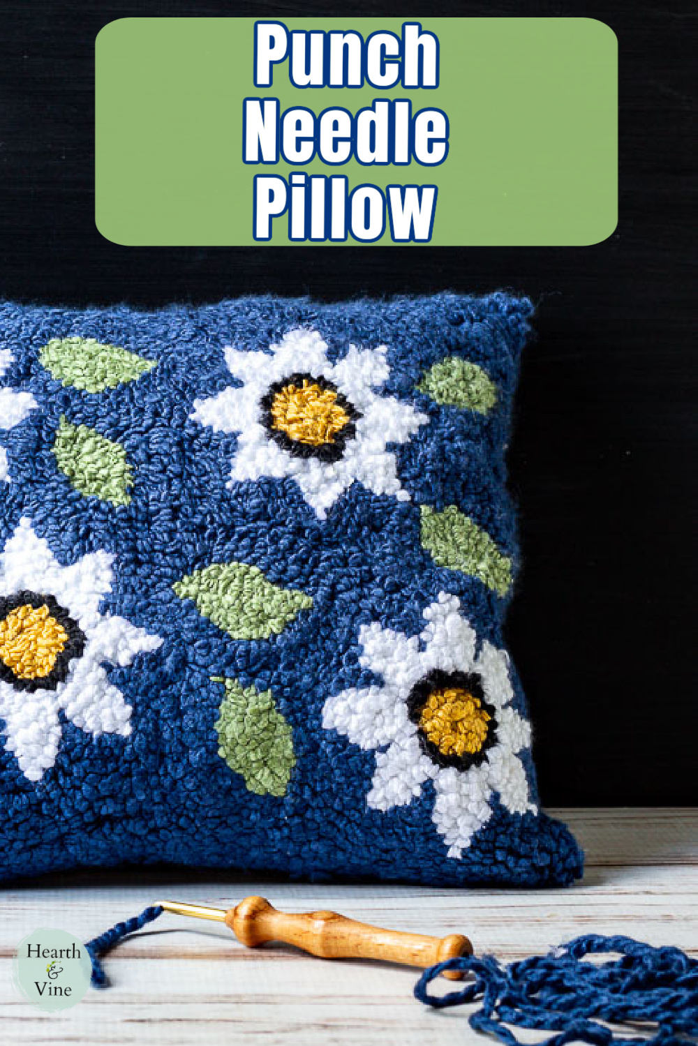 Blue with white daisy punch needle pillow and the needle with yarn below.