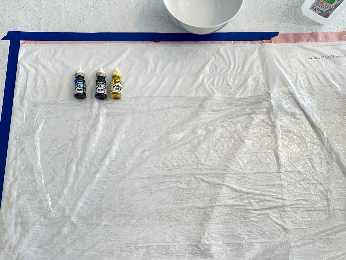Three alcohol ink bottles on plastic next to a piece of plastic wrap.