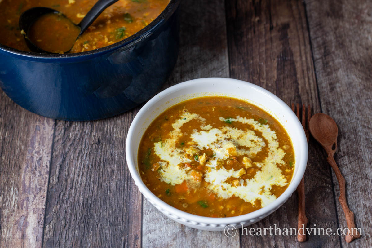 Bowl of chicken and butternut squash soup with a splash of cream next to a pot of the same soup.