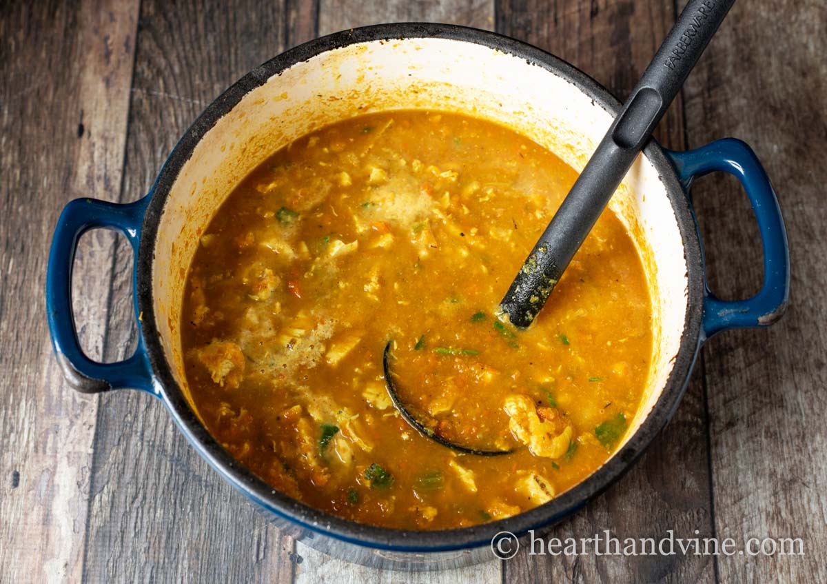 Large blue pot with butternut squash and chicken soup and a black ladel.