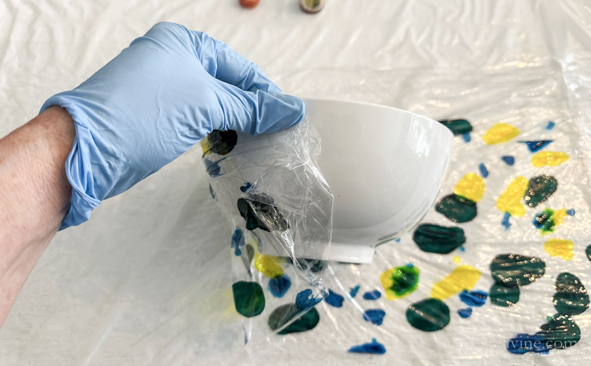Wrapping ink covered plastic wrap onto the outside of a white ceramic bowl.