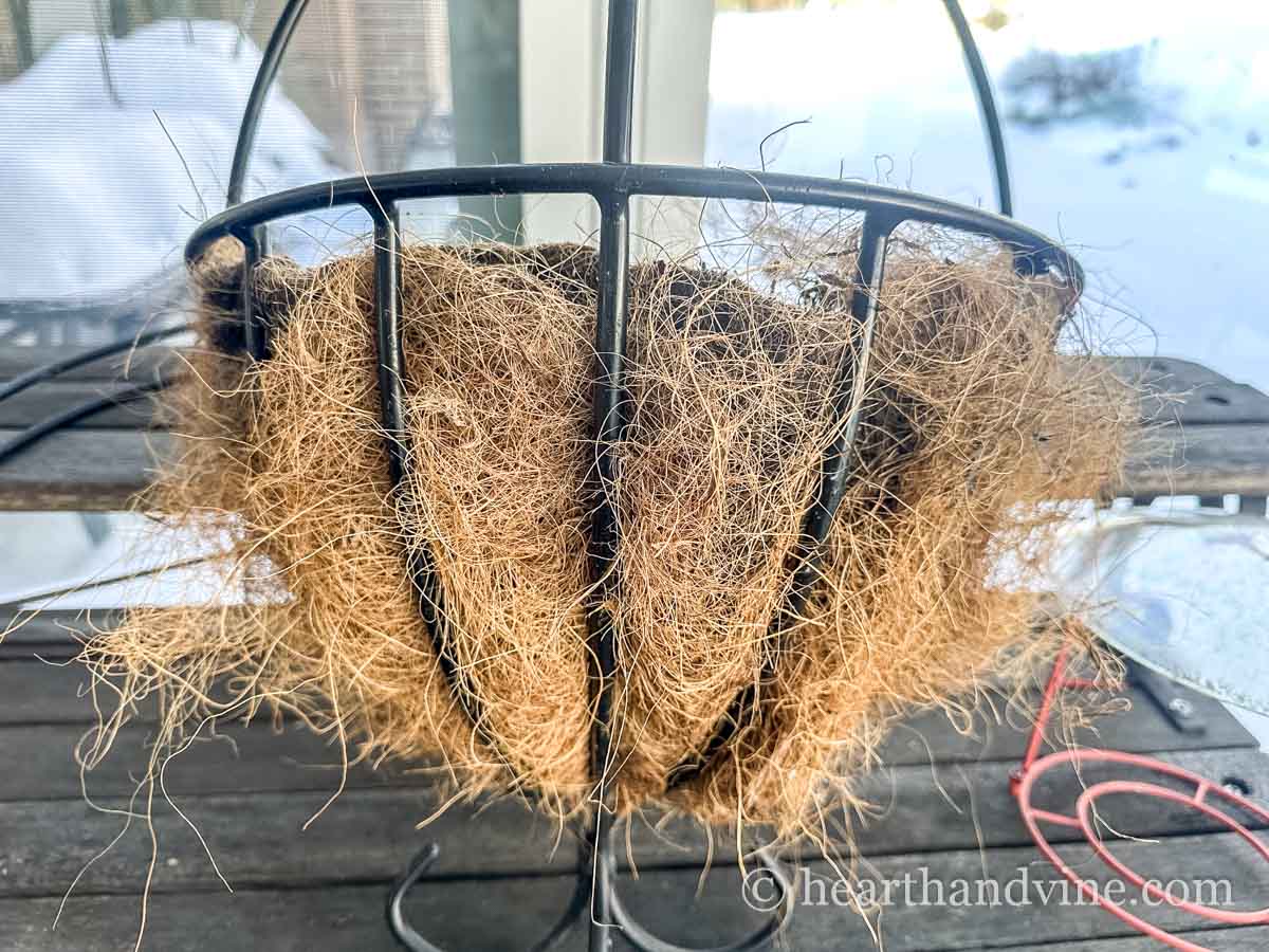 An empty hanging flower basket with a coco liner.