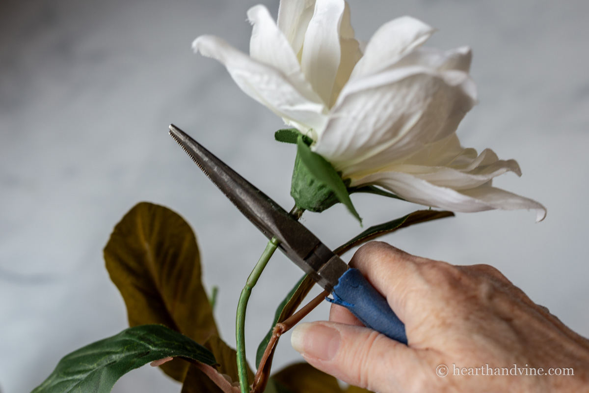 Wire cutters cutting off the bloom of an artificial magnolia flower.