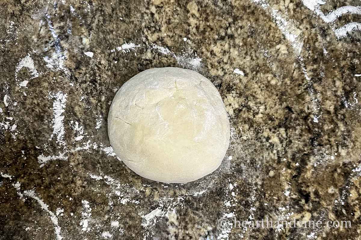 A ball of pizza dough on a light floured kitchen counter.