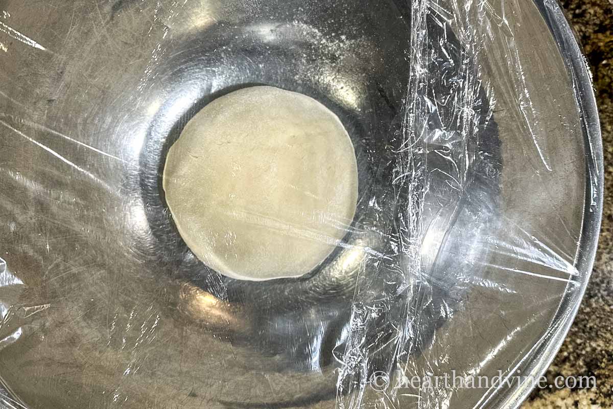 A ball of pizza dough in a mixing bowl covered with plastic wrap.