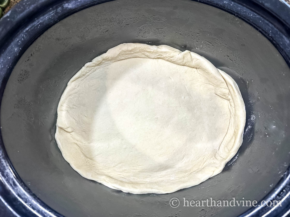 Raw pizza dough inside of a slow cooker with the edges of the crust up the sides.