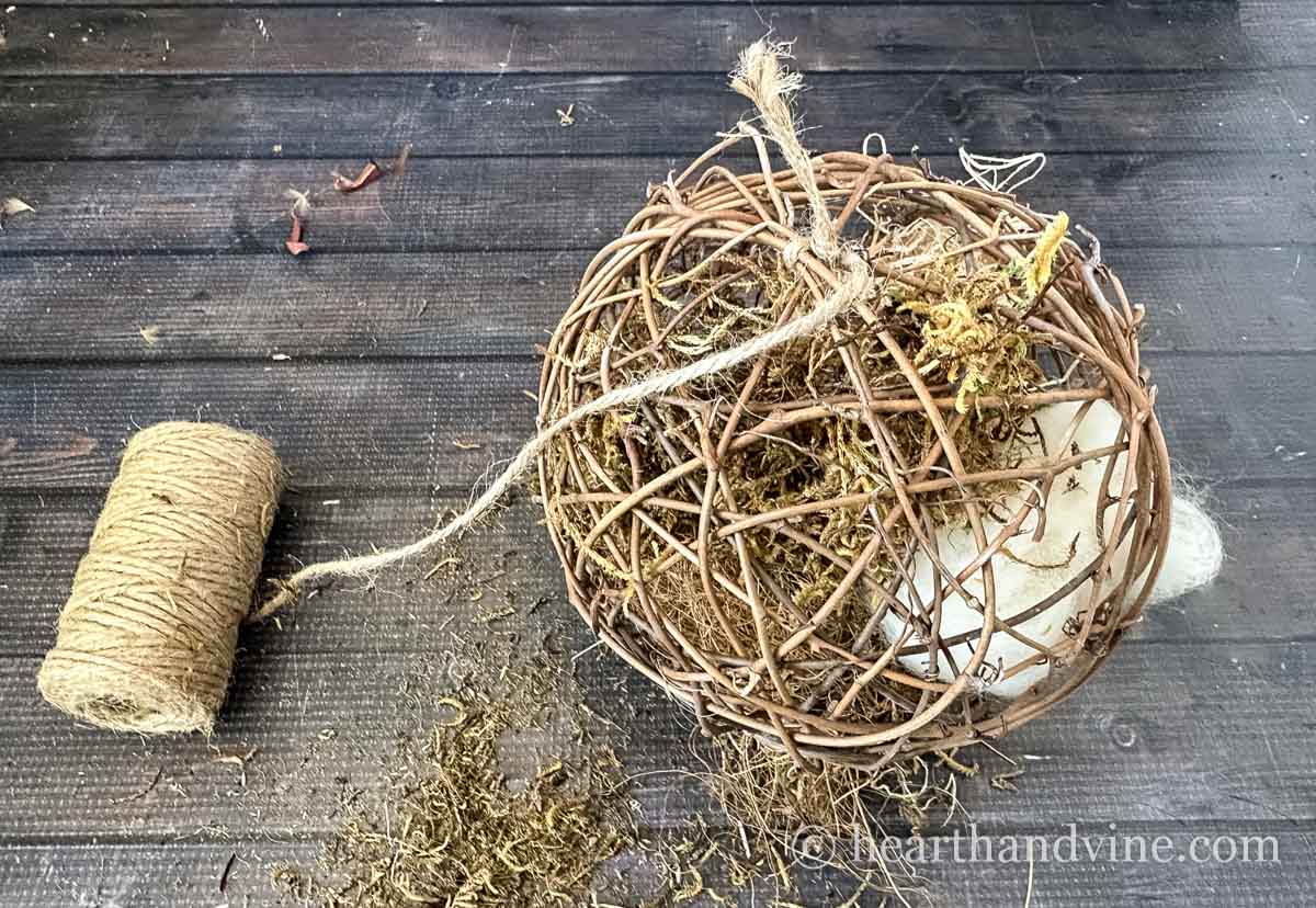 A spool of twine tied to a grapevine ball filled with moss and roving wool.
