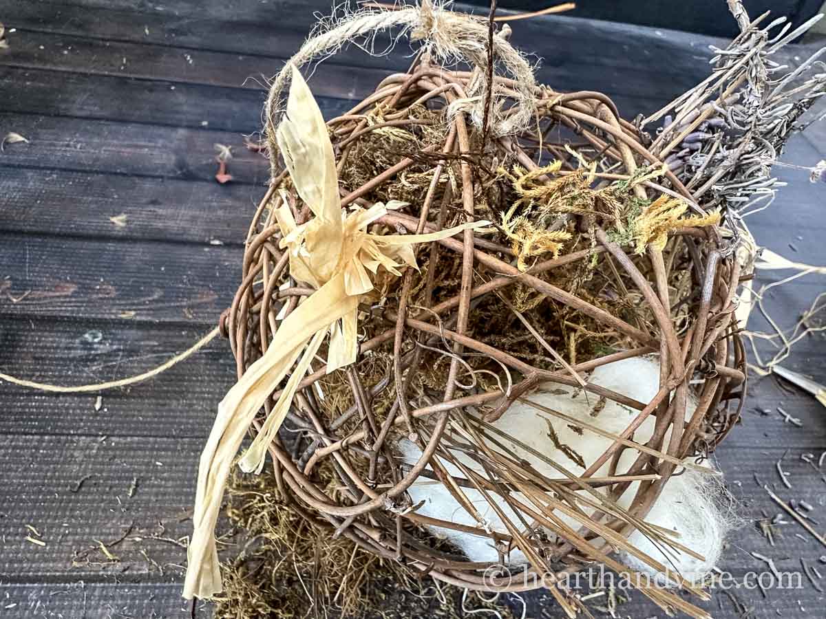 A grapevine sphere with raffia, twigs, moss and wool inside.