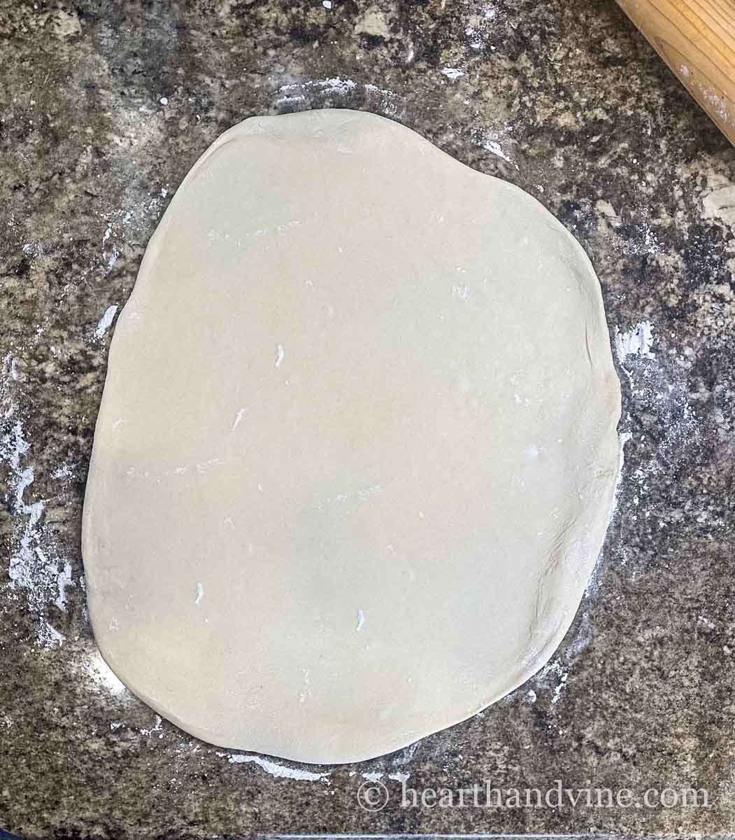 Raw pizza dough rolled out in a large oval.