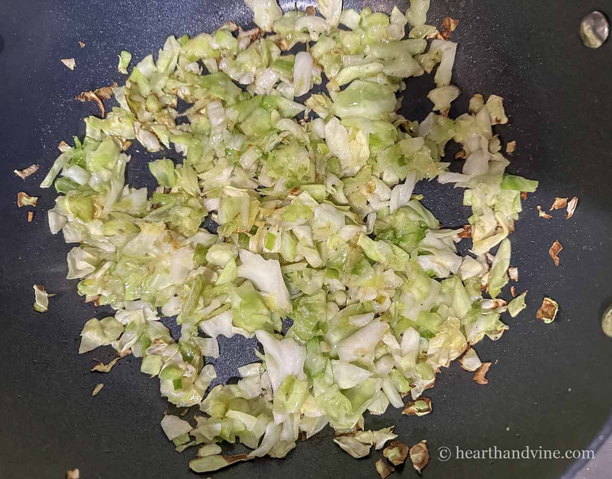 Green cabbage and scallions sauteed in a frying pan.