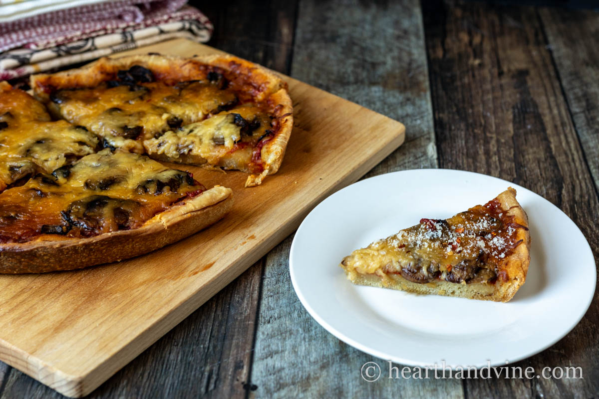 A slow cooker pizza on a wooden cutting board next to a slice on a white plate.