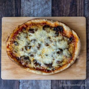 Slow cooker pizza with mushrooms and cheese on a wooden cutting board.