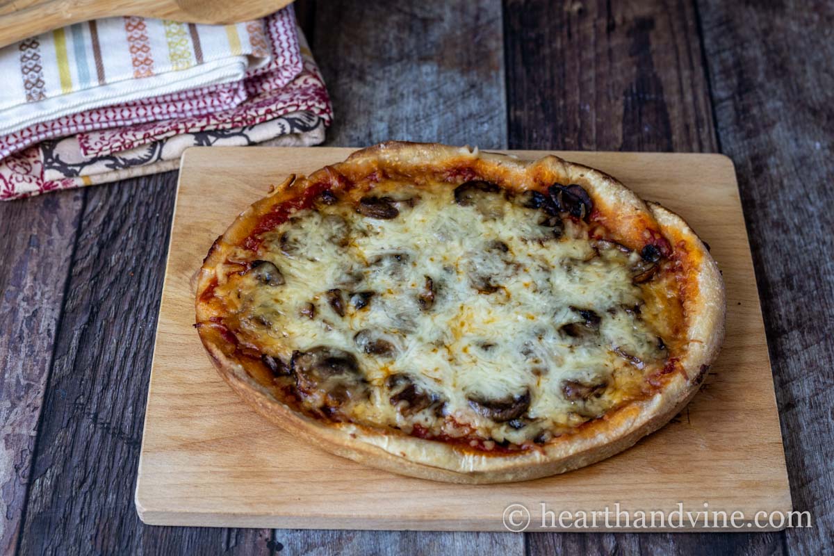A slow cooker pizza on a wooden cutting board.