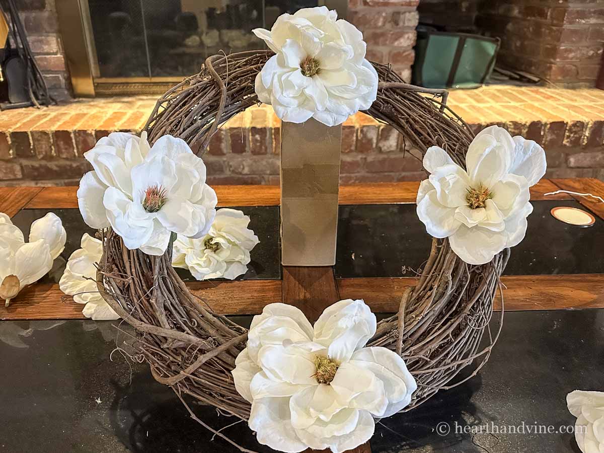 Four white magnolia flowers glued onto a grapevine wreath at north, south, east and west intervals.