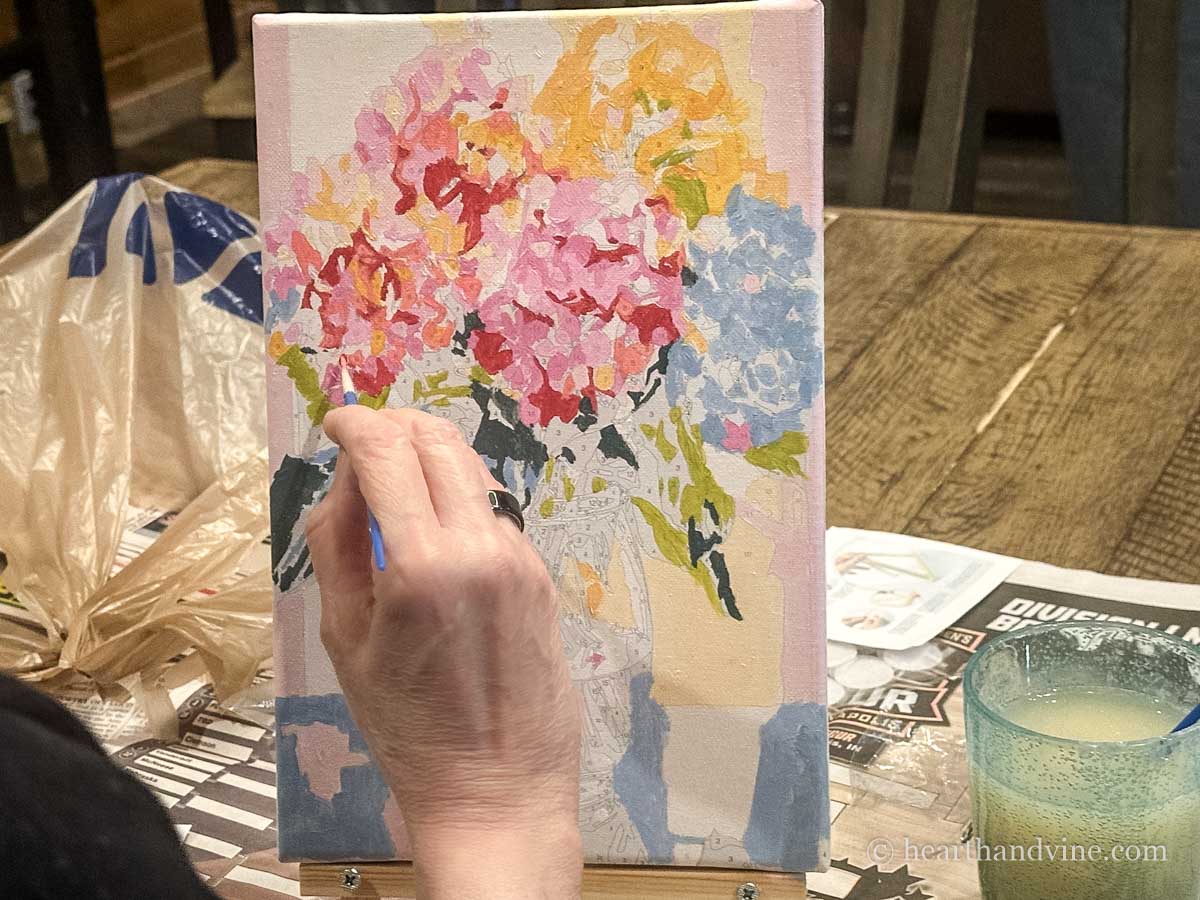 A hand painting the paint by numbers print of a vase of hydrangeas.