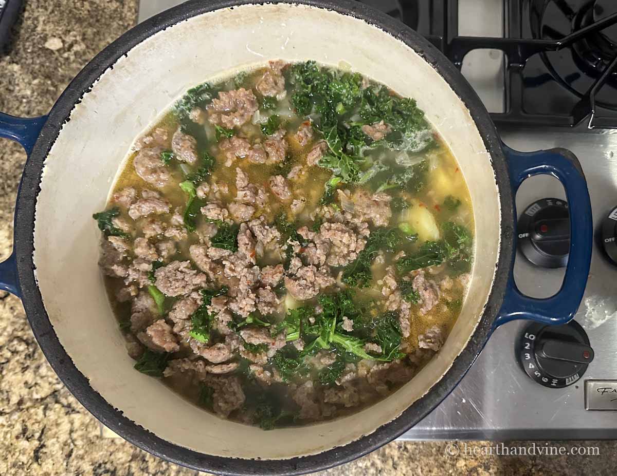 A Dutch oven pot on the stove with zuppa toscana soup.
