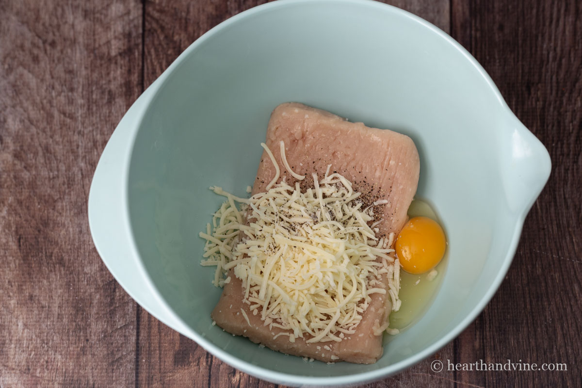Ground chicken, egg, salt, pepper and shredded mozzarella cheese in a bowl.