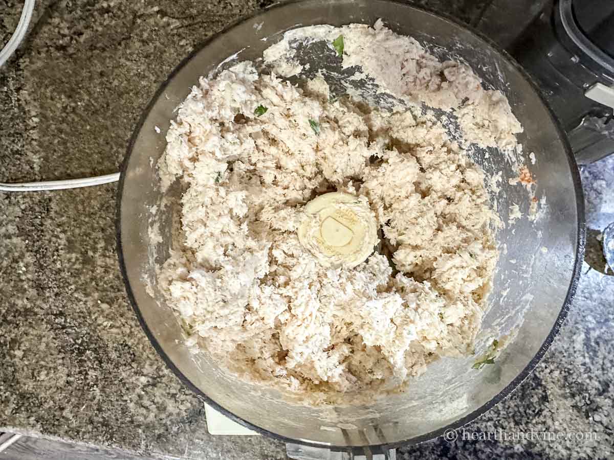 Chicken, cheeses and spices blending into a spread in a food processor.