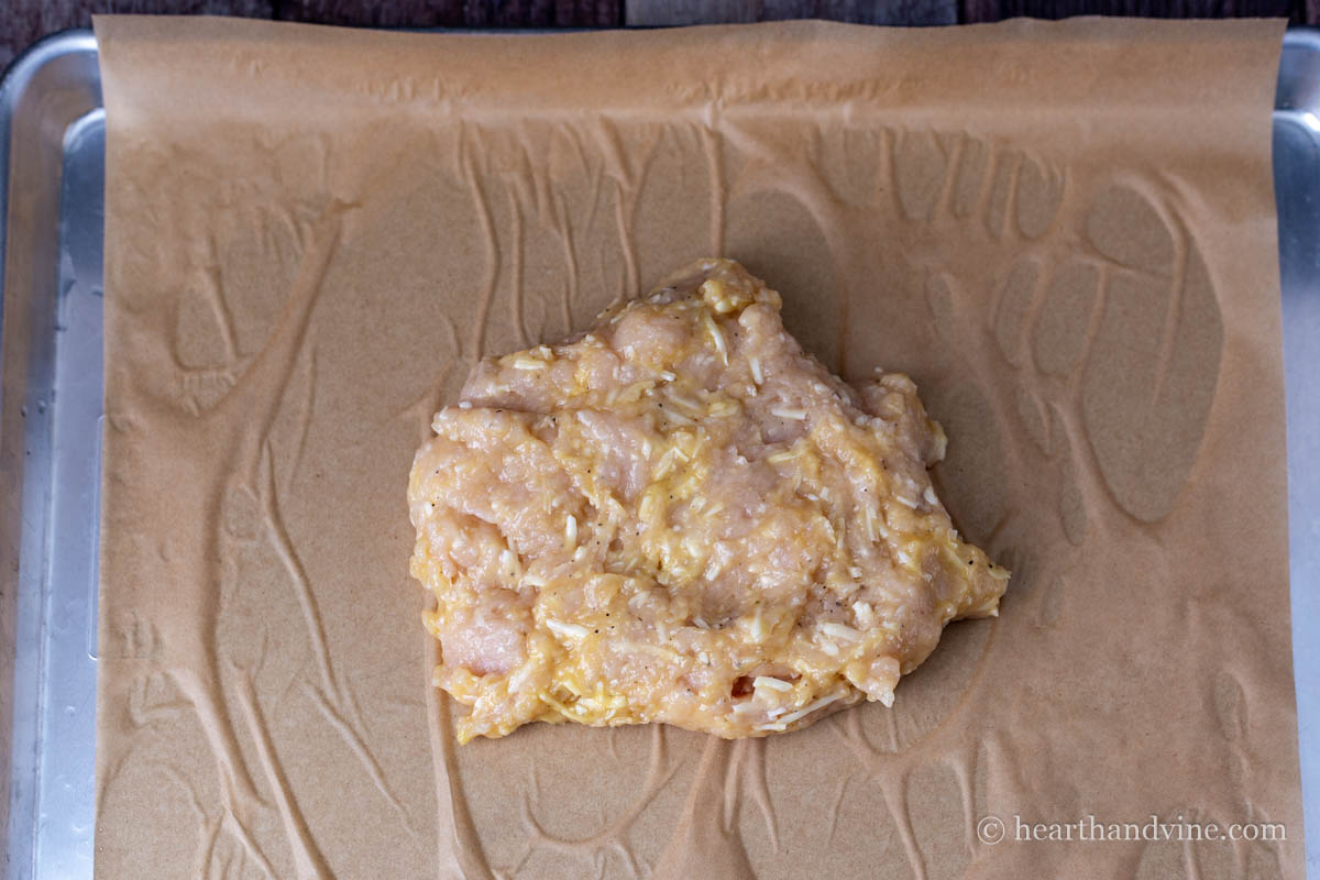 Chicken, egg, and cheese mixture on parchment on a baking pan.