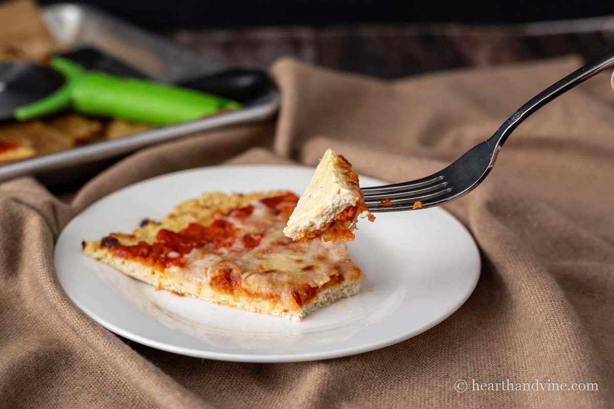 A fork lifting a bit of chicken parm pizza from a slice on a white plate.